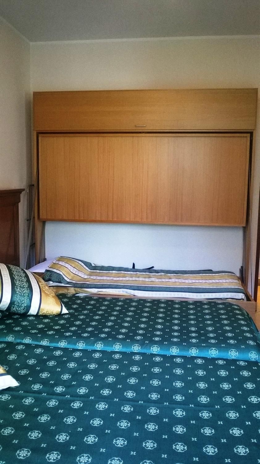 Een slaapkamer met een houten hoofdbord, een bed met beddengoed met een patroon en een nachtkastje met een lamp.