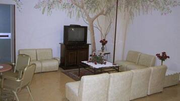 A living room with a sofa, armchair, TV stand, and a decorative tree mural on the wall.