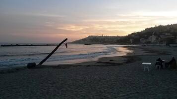 Una playa con una estructura de madera, una silla blanca y una persona sentada sobre la arena.