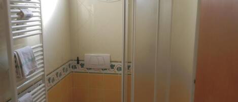 A compact bathroom with a toilet, a sink, a shower enclosure, and a towel rack.