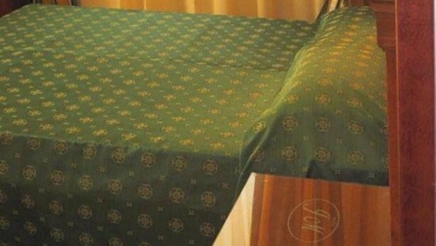 Una cama con una colcha verde estampada y un cabecero de madera.