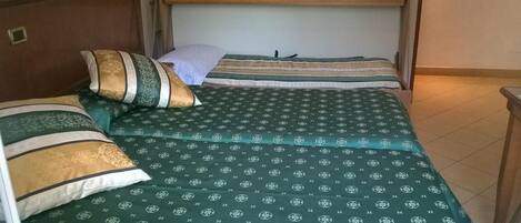 A single bed with a green patterned bedspread and two pillows, one with a striped design and another with a solid color.