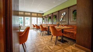 A restaurant with wooden flooring, orange chairs, and a green wall.
