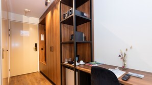A compact office space with a wooden desk, a black chair, a small refrigerator, and a bookshelf. - HOTEL HERIKERBERG (Markelo)