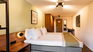 A hotel room with a large bed, a wooden bench, a desk, and a mirror. - HOTEL HERIKERBERG (Markelo)