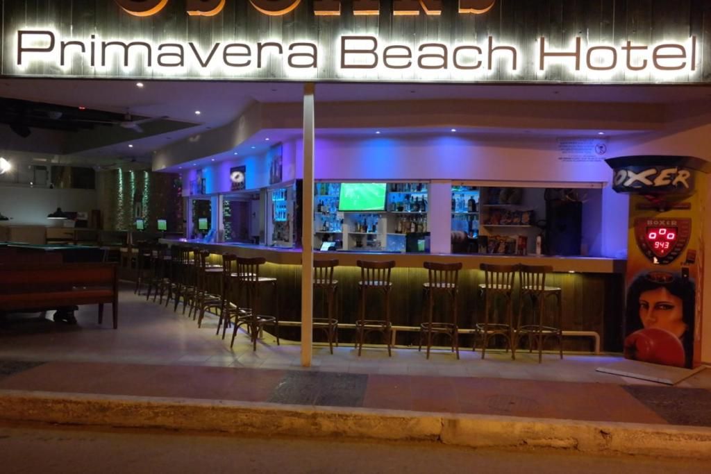 Zona bar con insegna luminosa per l'hotel Primavera Beach, sgabelli da bar e uno schermo televisivo.