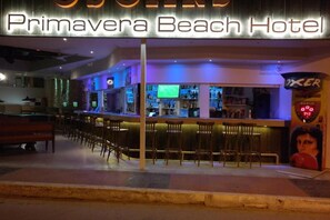 A bar area with a neon sign for Primavera Beach Hotel, bar stools, and a television screen. - Primavera Beach Hotel (Hersonissos)