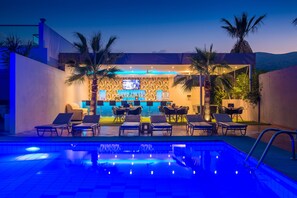 A poolside bar area with lounge chairs, a bar counter, and a television screen. - Primavera Beach Hotel (Hersonissos)