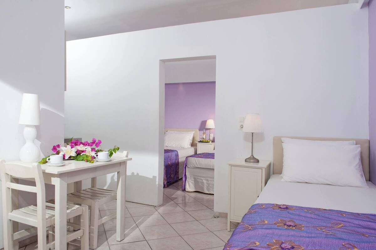 A hotel room with a bed, a desk with a chair, a nightstand with a lamp, and a small table with flowers.