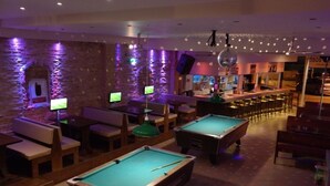 Een biljartkamer met twee pooltafels, zitplaatsen en een bar.