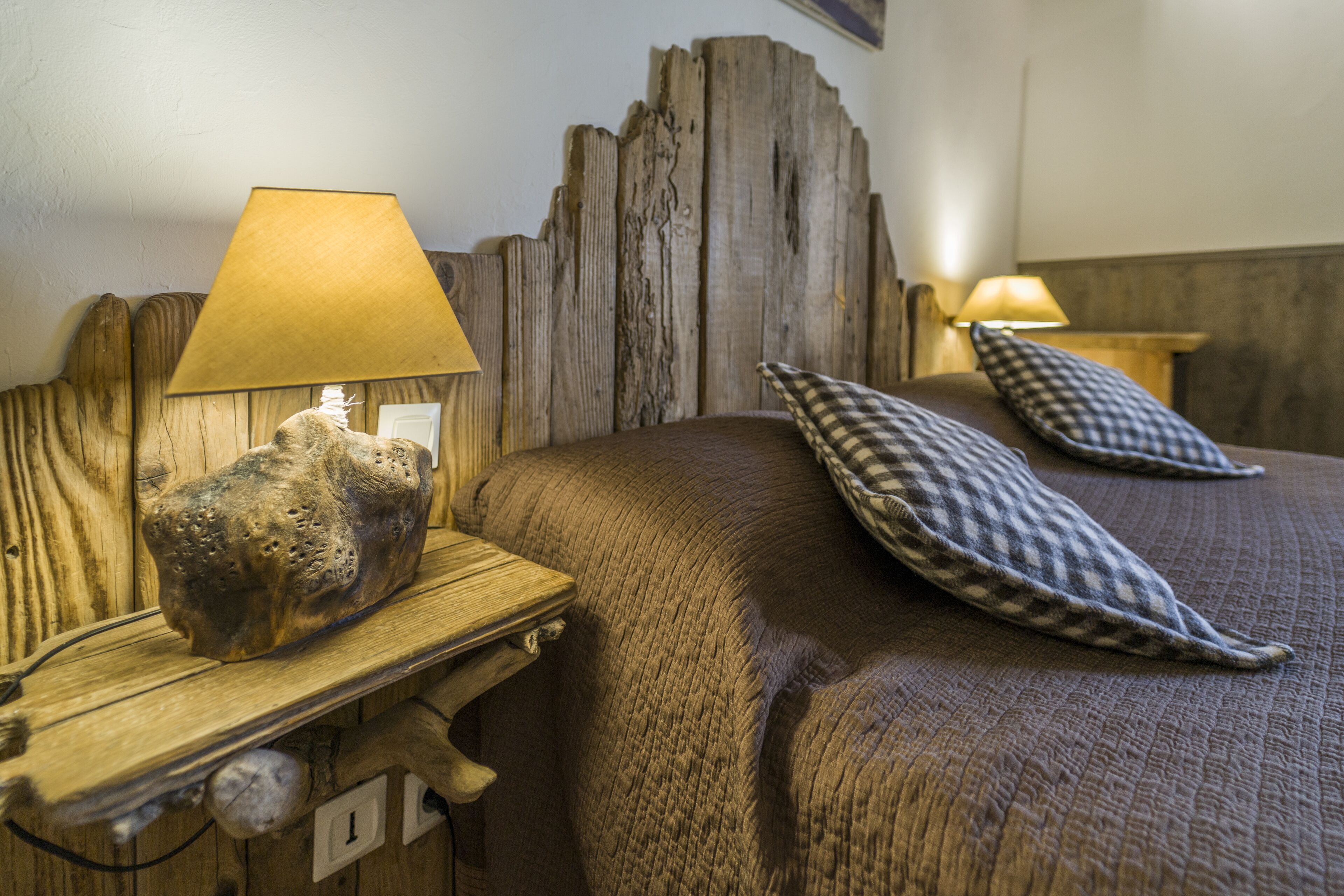 A wooden headboard with a rustic finish, a bedside lamp, and two checkered pillows on a bed.