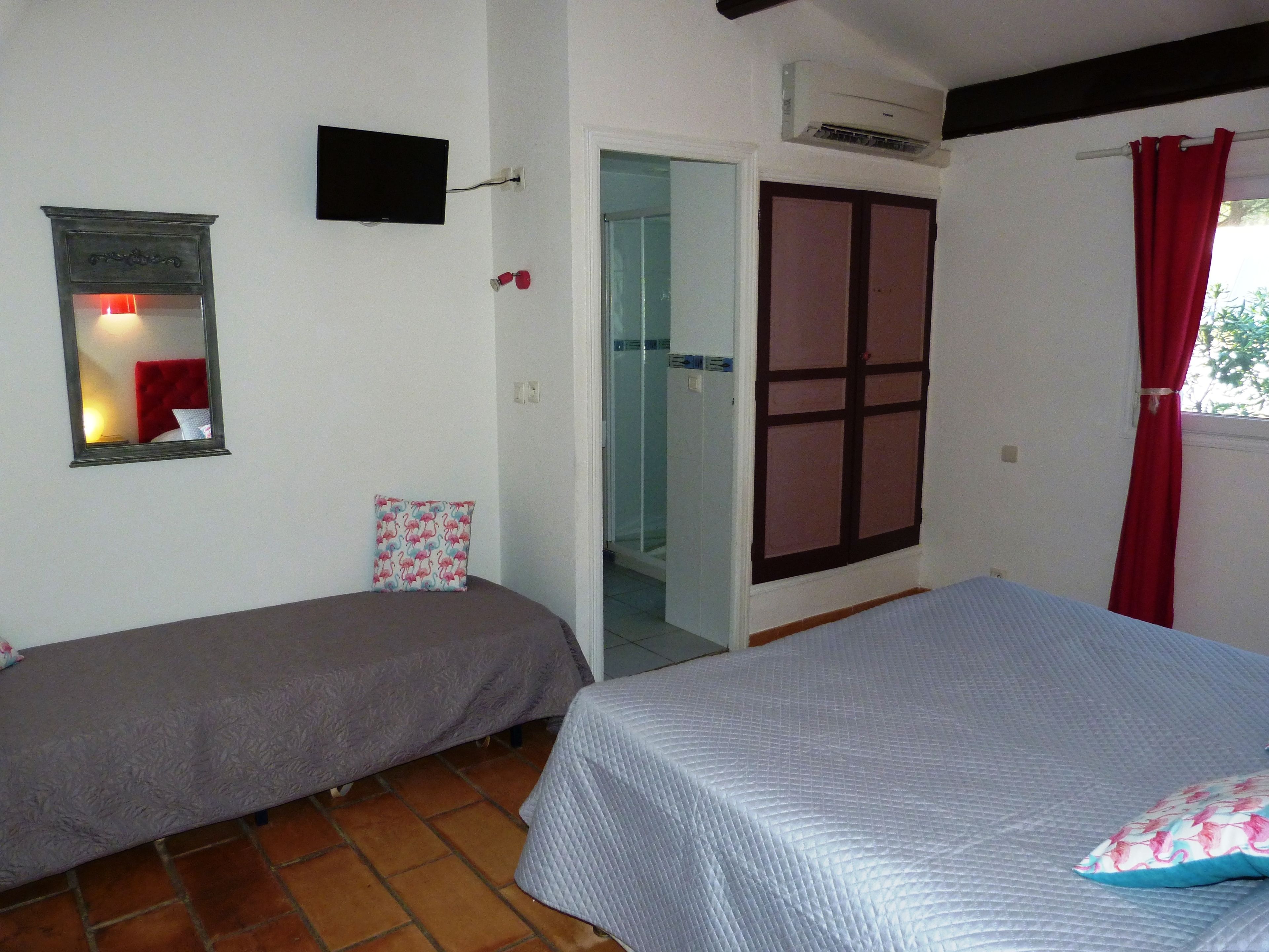 Quarto com duas camas de solteiro, uma televisão fixada na parede, um aparelho de ar condicionado e uma porta que dá para outro cômodo.