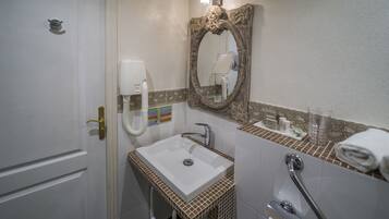 Une salle de bain avec un lavabo blanc, un miroir doté d’un cadre orné, un porte-serviettes et un sèche-mains.