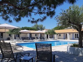 Zona de piscina con sillones reclinables y sombrillas, rodeada de edificios con techos de tejas.
