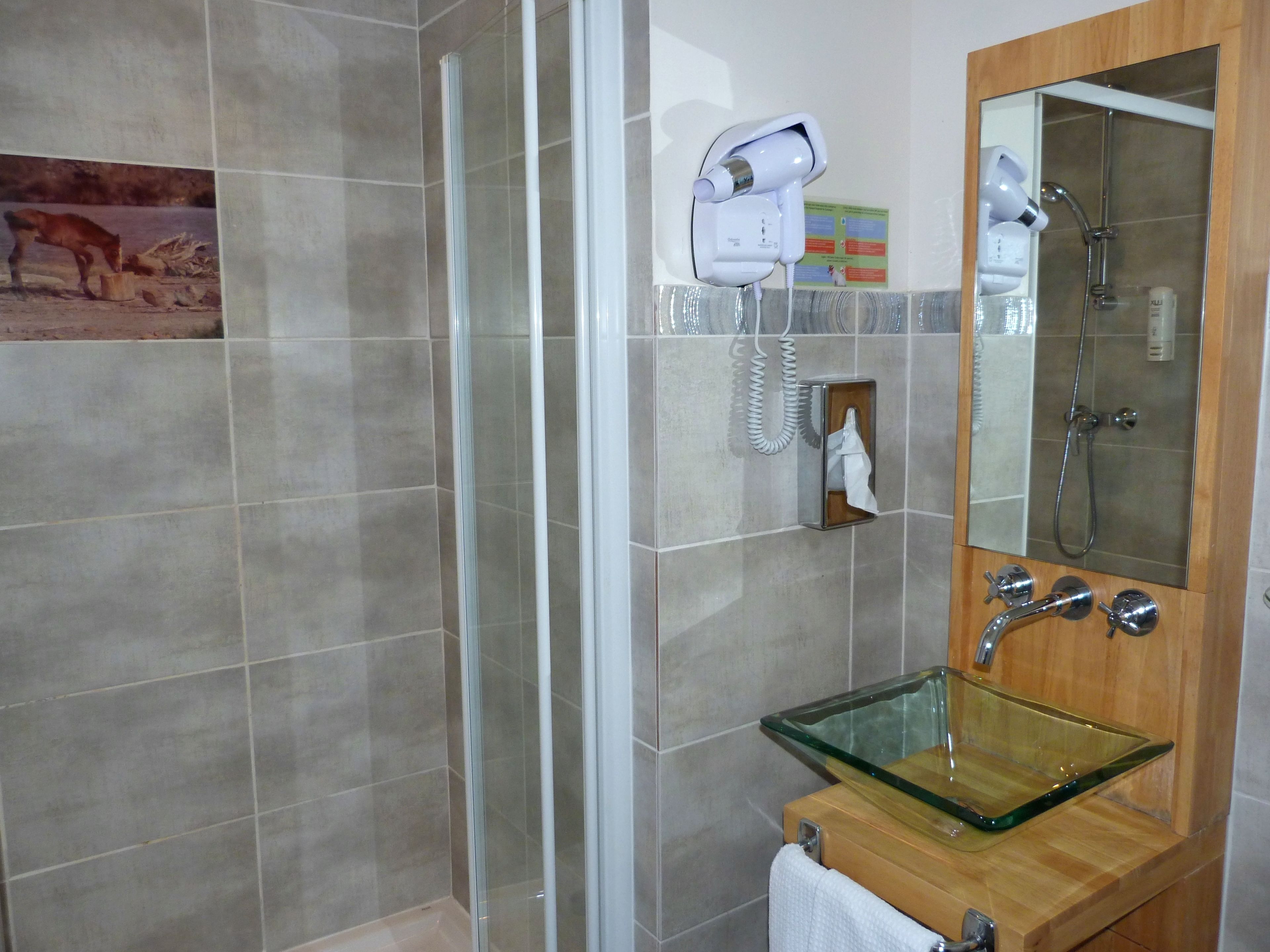 Un baño con lavamanos de vidrio, un espejo, toallero y secador de pelo montado en la pared.