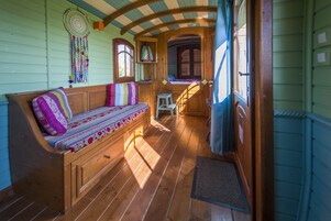 Interior acogedor de una cabaña con un banco de madera, un taburete pequeño y una ventana con contraventanas de madera.