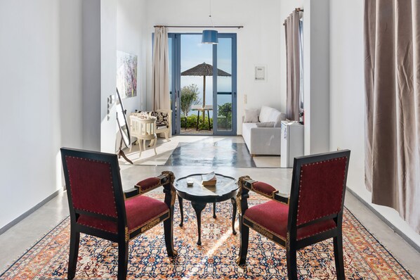 A room with a large window, a dining area with a table and chairs, a sofa, and a view of the sea.