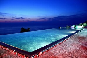 An infinity pool with a clear view of the ocean at dusk.