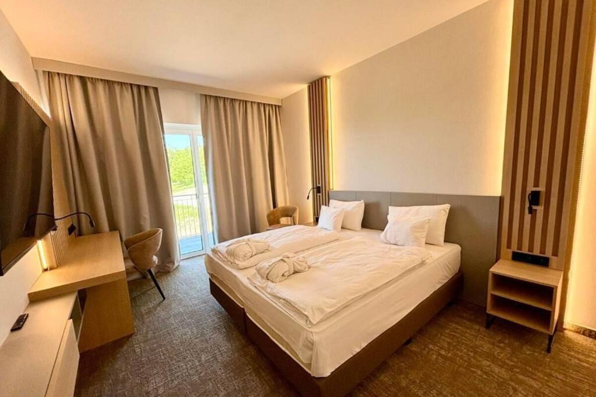 A hotel room with a large bed, a desk, a chair, and a TV.
