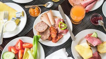 A breakfast setting with plates of food, including meats, cheese, and vegetables, and a glass of orange juice.