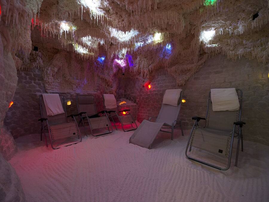 Uma gruta com área de estar, com poltronas e uma mesa pequena, iluminada por luzes coloridas.