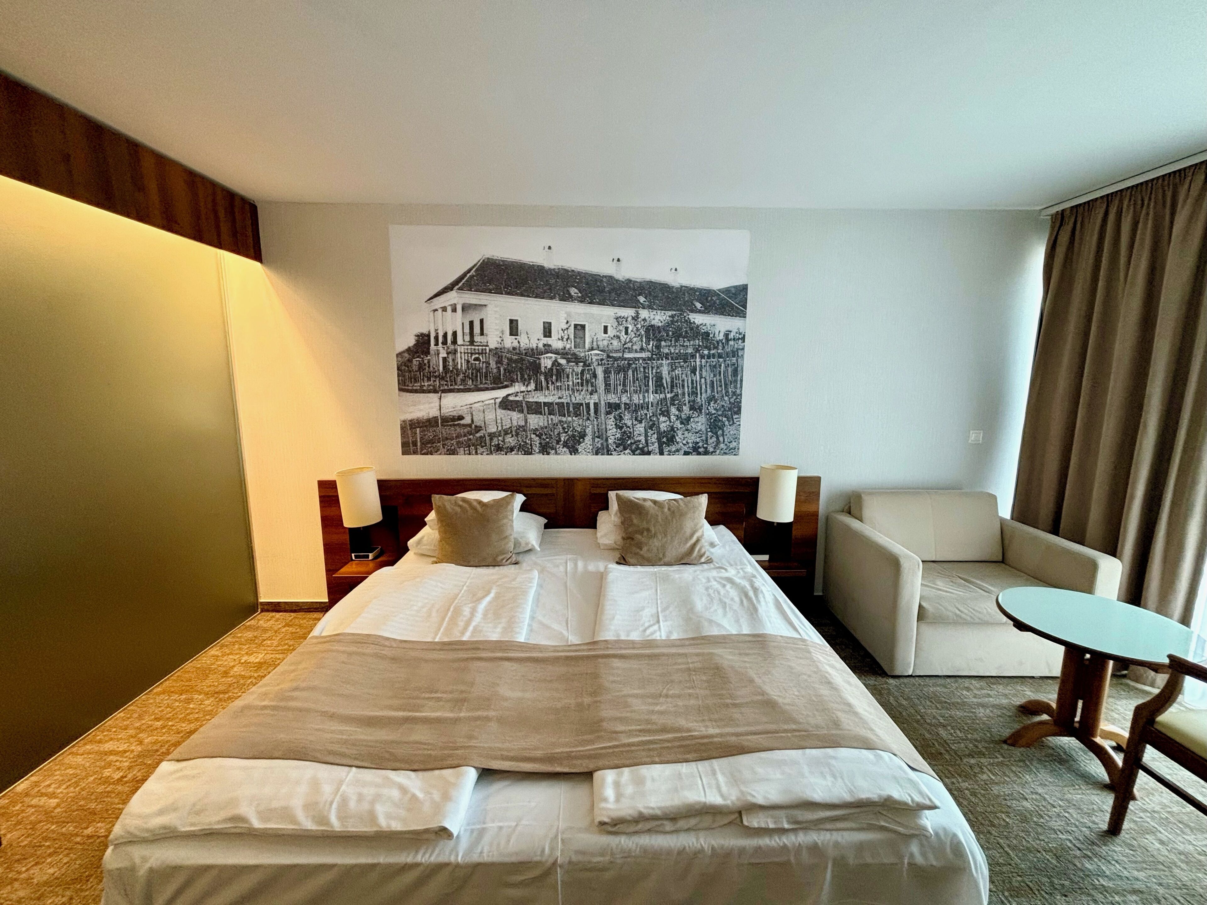 Una habitación de hotel con una cama grande, una silla, una mesita y un cuadro colgado en la pared.