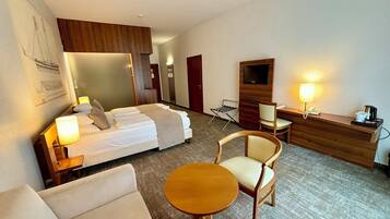 Habitación de hotel con cama, sofá, una mesita redonda, escritorio con silla, televisor y lámpara.