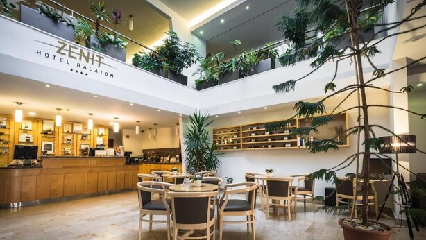 A hotel lobby with a reception desk, seating area, and indoor plants. - Zenit Hotel Balaton (Vonyarcvashegy)