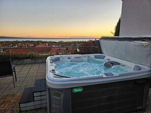 A hot tub with a view of a residential area and a body of water during sunset. - Zenit Hotel Balaton (Vonyarcvashegy)