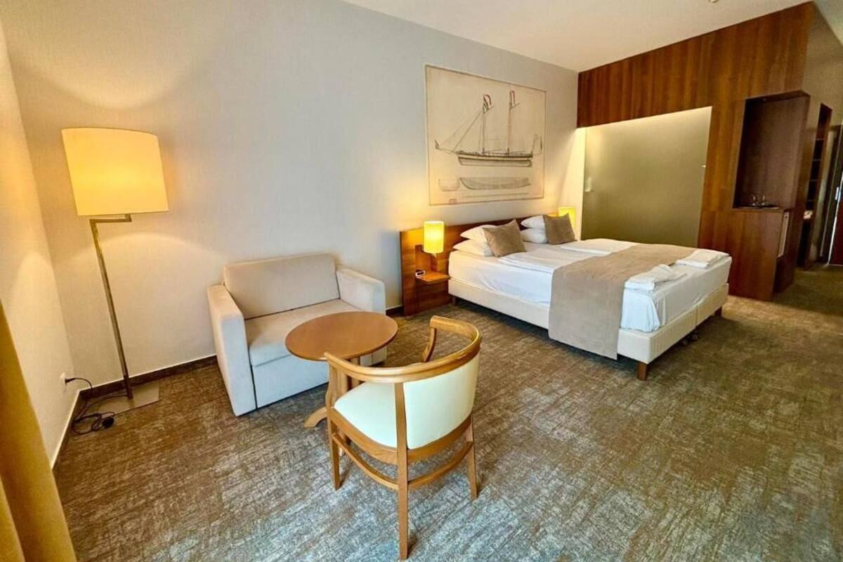 A hotel room with a bed, a desk, a chair, a lamp, and a painting on the wall.