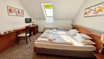 A hotel room with a bed, desk, chair, and artwork on the walls.