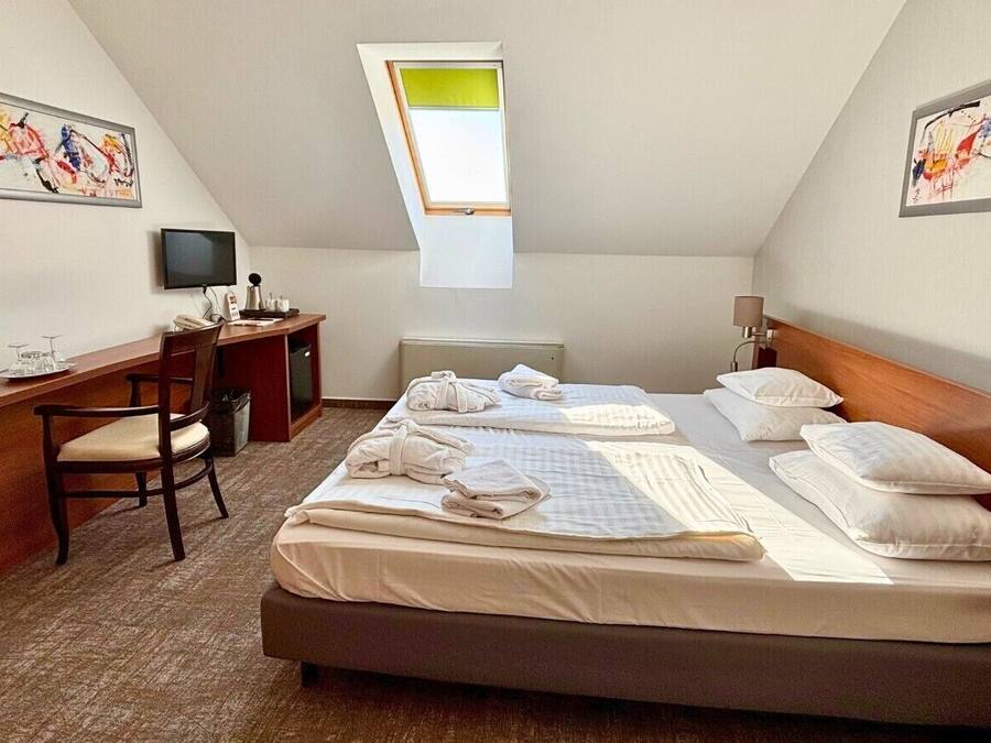 A hotel room with a bed, desk, chair, and artwork on the walls.