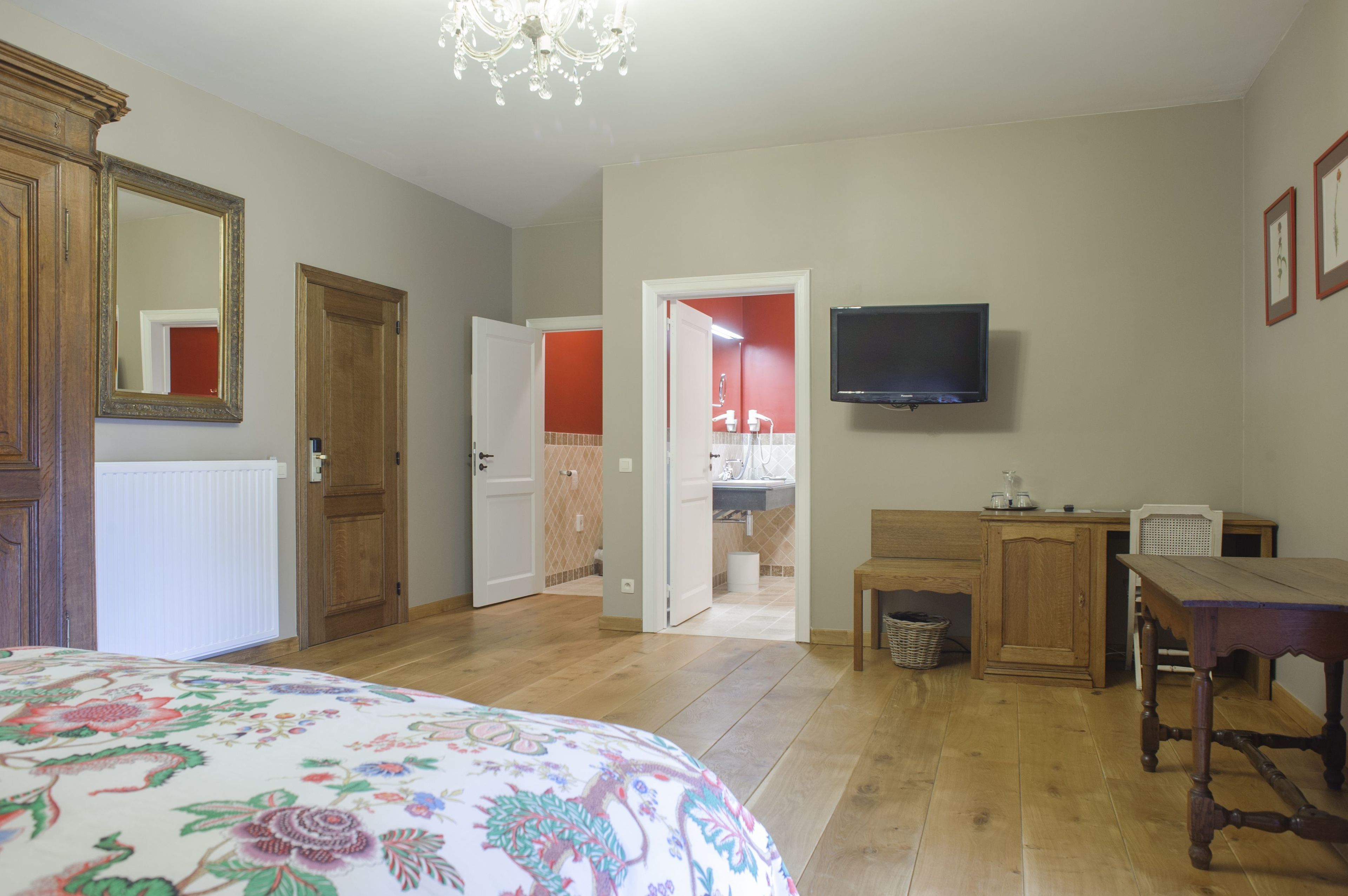 A bedroom with a large bed, wooden furniture, a television, and a bathroom visible through an open door.