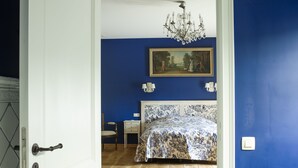 A bedroom with a bed, a chair, a nightstand, a painting on the wall, and a chandelier. - Kamerijck Bed & Breakfast (Gingelom)