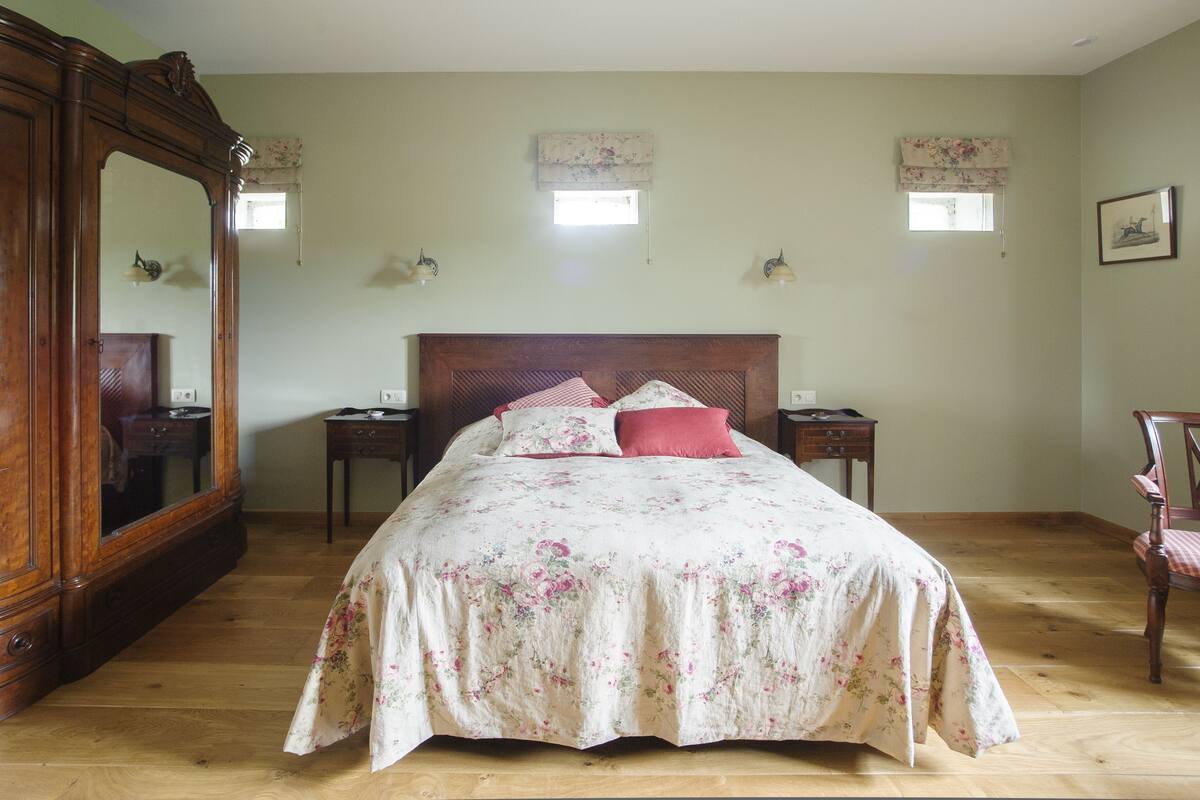 Een slaapkamer met een groot houten bed, een dressoir, twee nachtkastjes en een stoel.