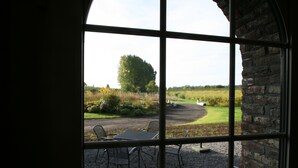 A view through a window with a table and chairs outside, a brick wall, and a grassy field with trees. - Kamerijck Bed & Breakfast (Gingelom)