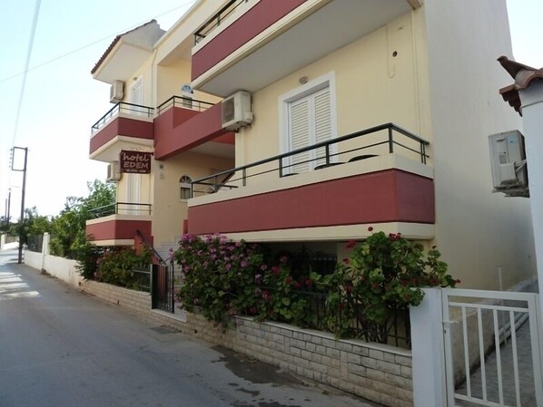 A two-story hotel with a red and beige facade, balconies, and a sign indicating it is a hotel.