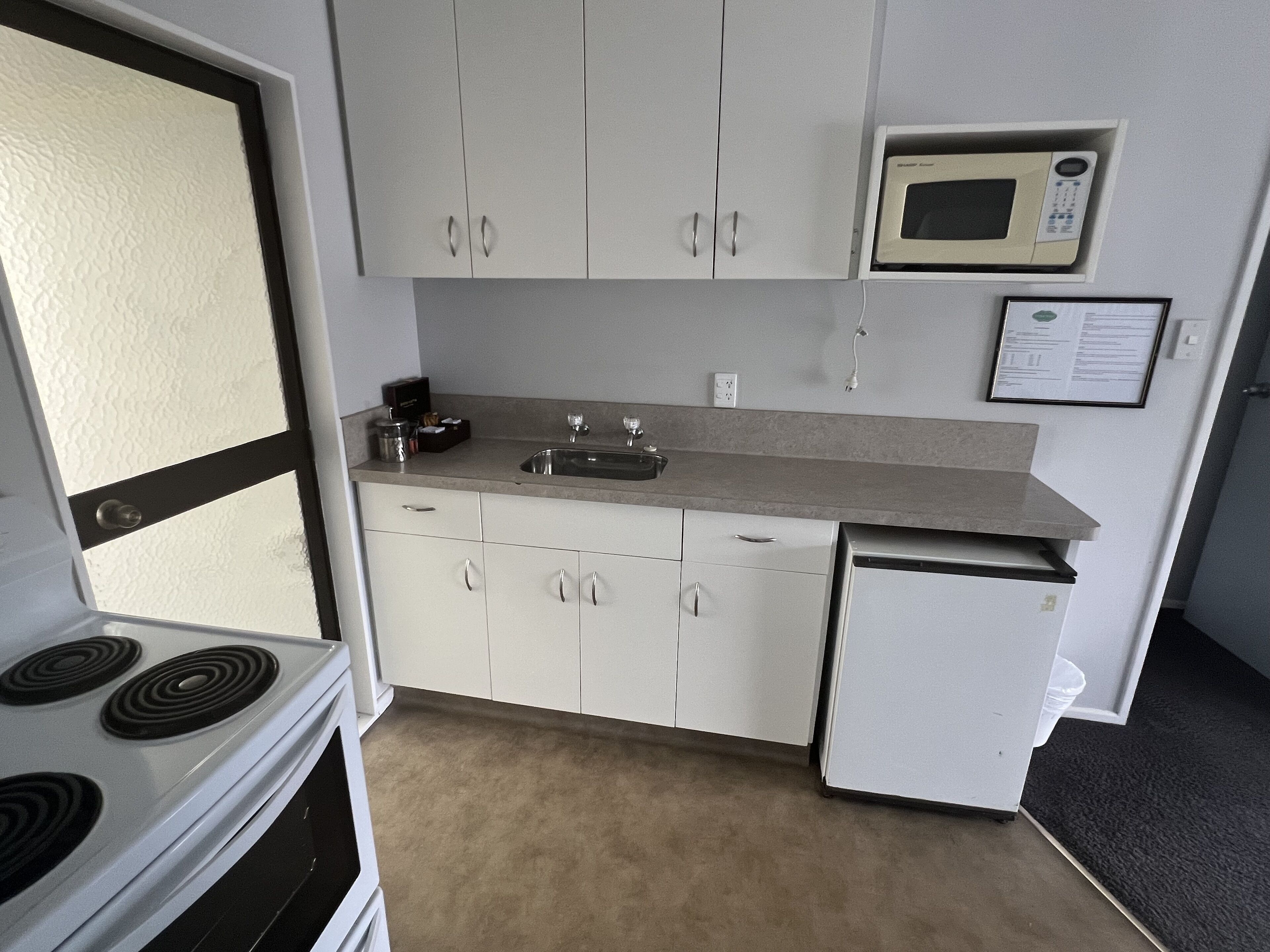 A compact kitchen with white cabinets, a microwave, a stove, and a sink.