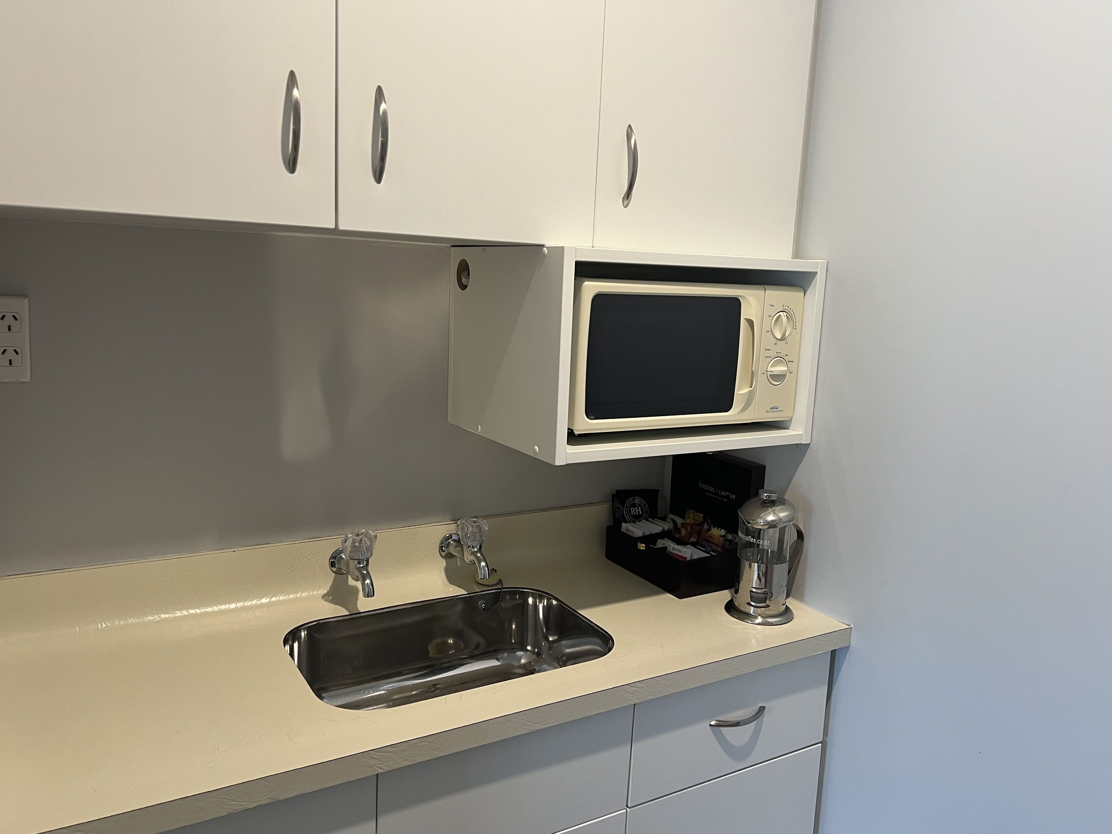 Cocina con encimera blanca, pileta, microondas y alacenas.