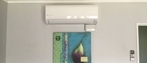 A room with a white air conditioner mounted on the wall, a colorful artwork depicting a teardrop shape, and a door with a lock.