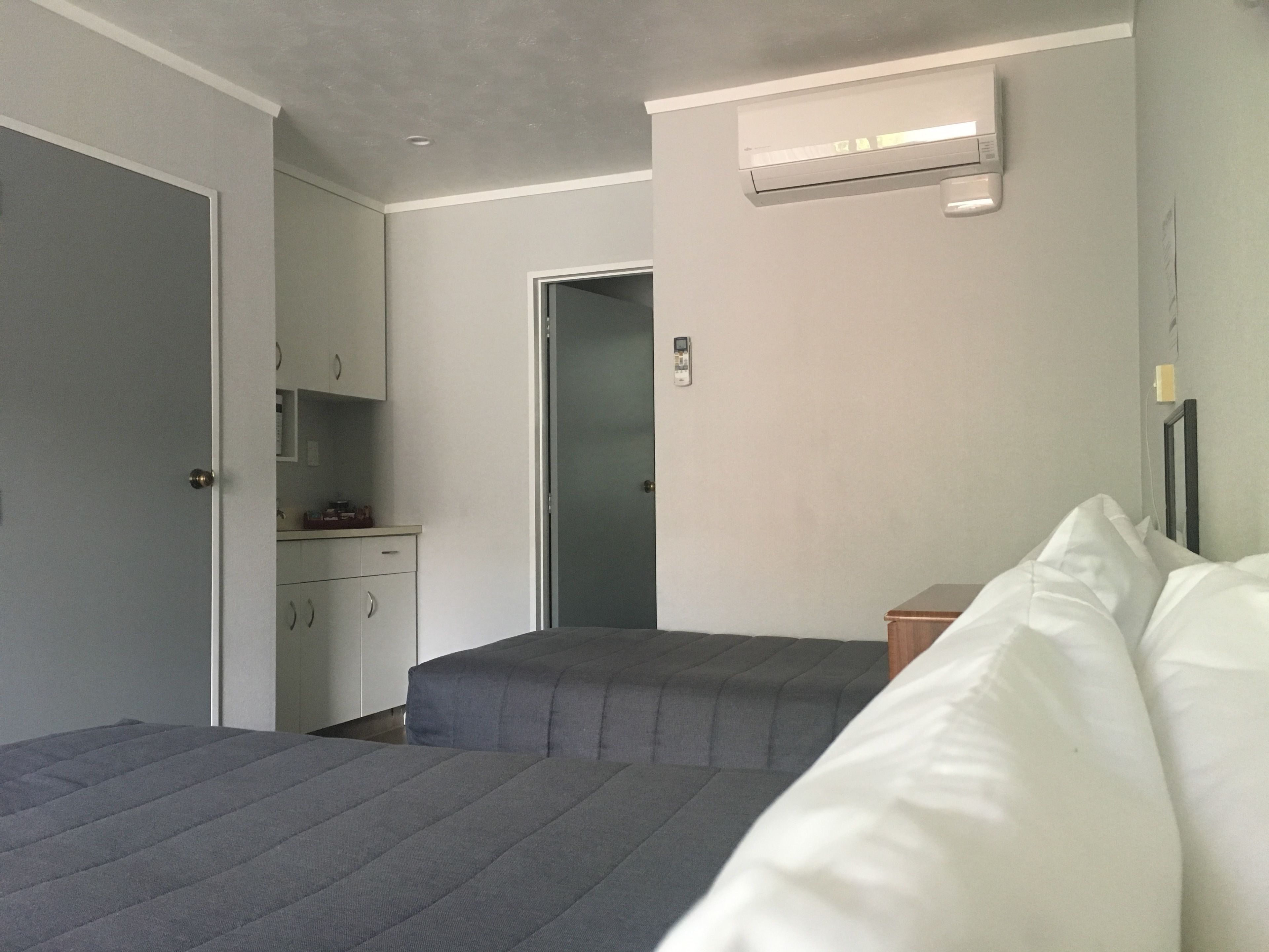 Un dormitorio con dos camas, una mesita de noche pequeña, un armario y un equipo de aire acondicionado en la pared.