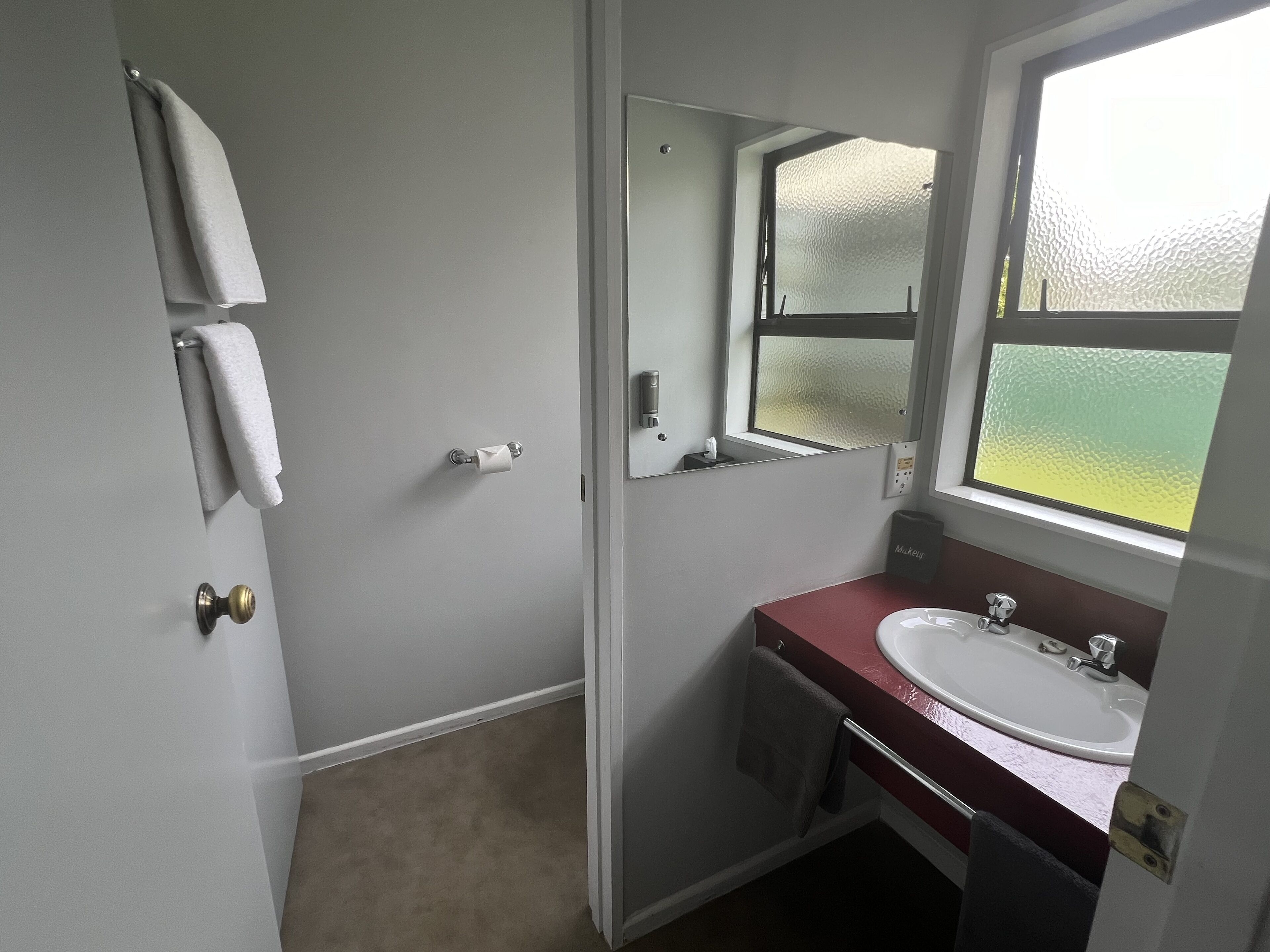 Een badkamer met een witte deur, een spiegel, een wastafel en een handdoekhouder.