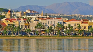 A coastal town with buildings, palm trees, and mountains in the background. - Casa Maistra Residence (Rethymno)