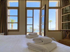 A hotel room with a bed, two windows, and a view of palm trees and a balcony. - Casa Maistra Residence (Rethymno)