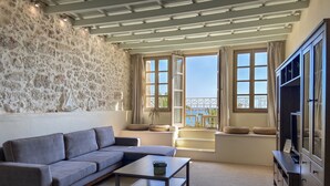 A living room with a stone wall, a grey sofa, a coffee table, and a TV cabinet. - Casa Maistra Residence (Rethymno)