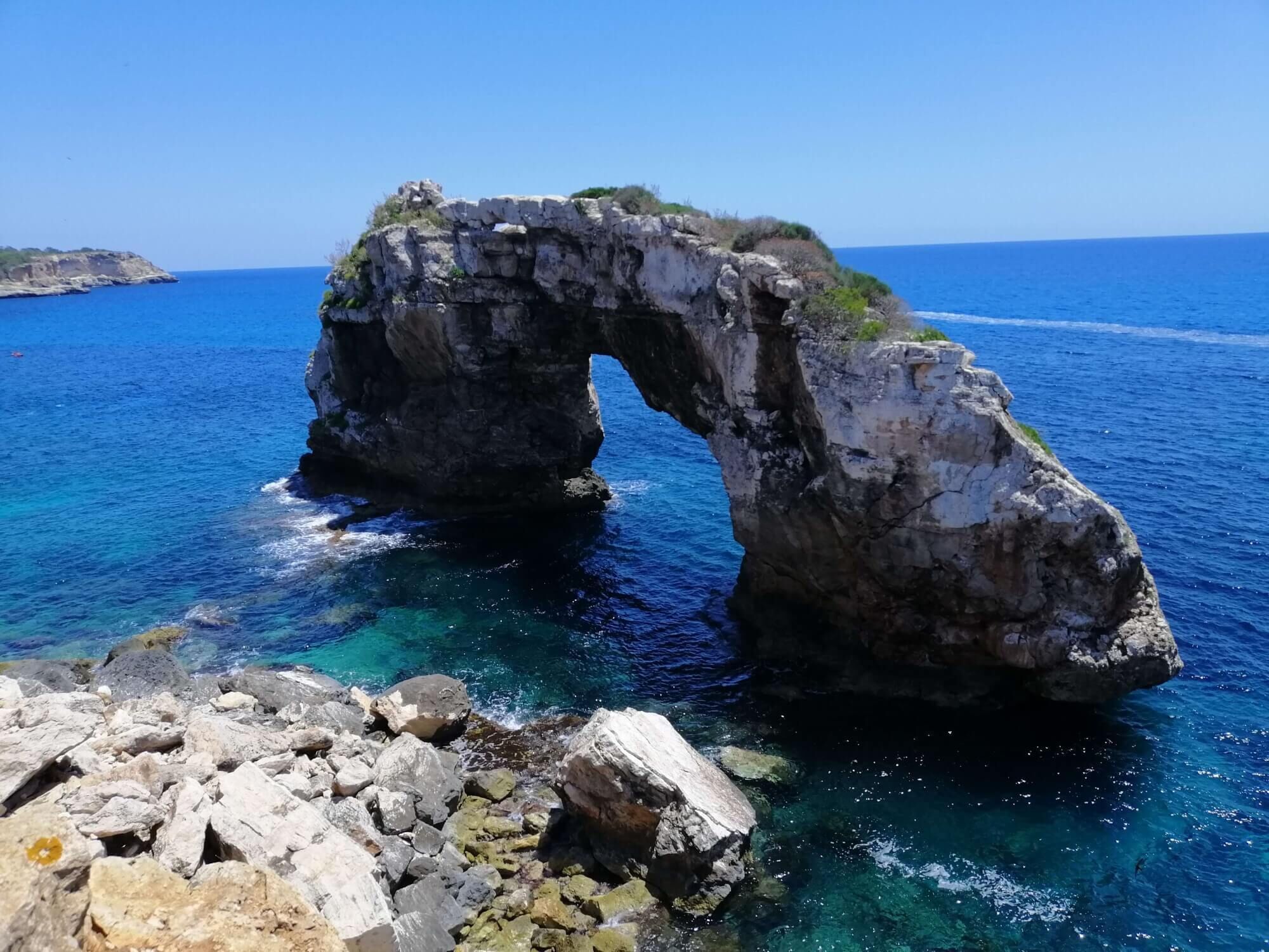A natural rock arch formation in clear blue waters.