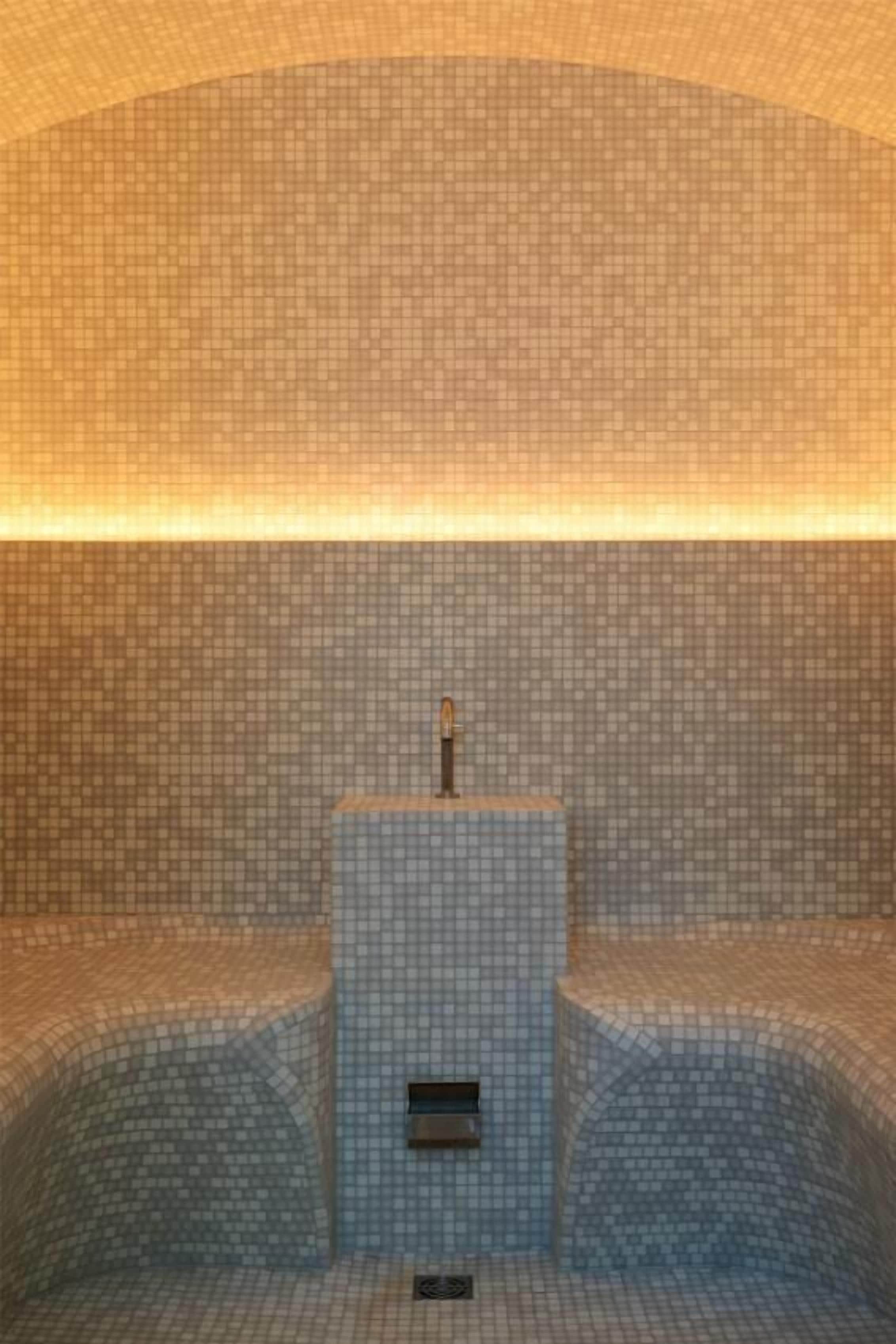 Une salle de bain avec un sol et des murs carrelés, un lavabo central et un espace douche.
