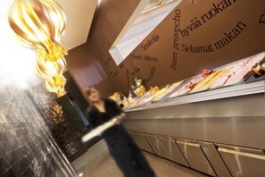 A person walking past a food display with various items and a wall with text in a foreign language. - Parkhotel (Kortrijk)