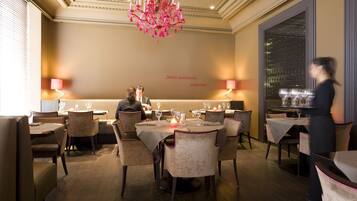 A formal dining room with tables set for two, elegant chairs, and a chandelier.