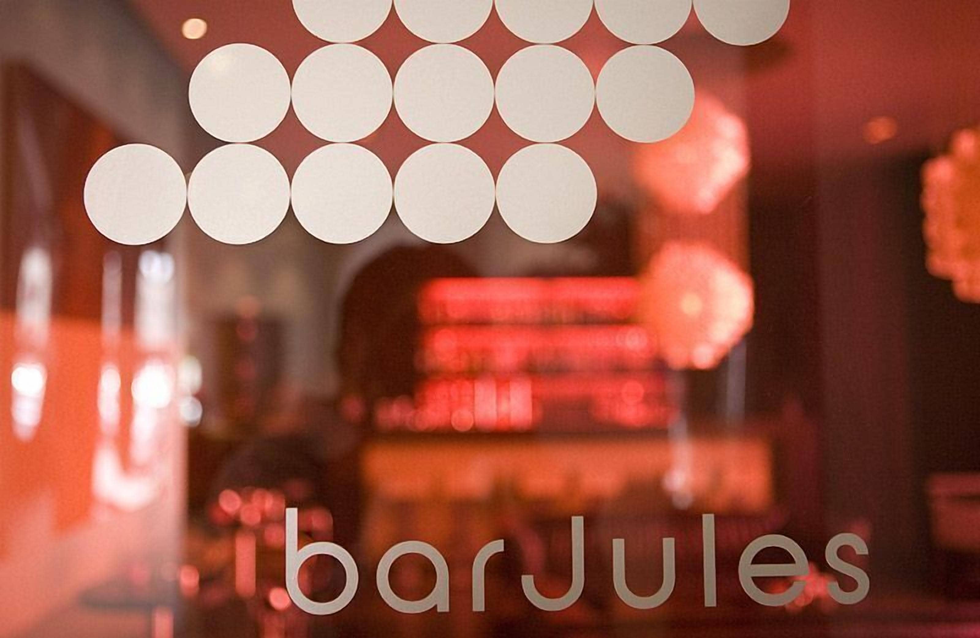 Um bar com uma luminária circular e o texto "barJules" na janela.